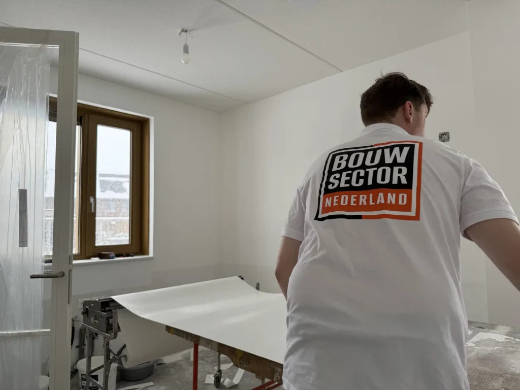 Behanger van Bouwsector Nederland rolt een baan behang uit over de plaktafel in een nieuwbouwkamer