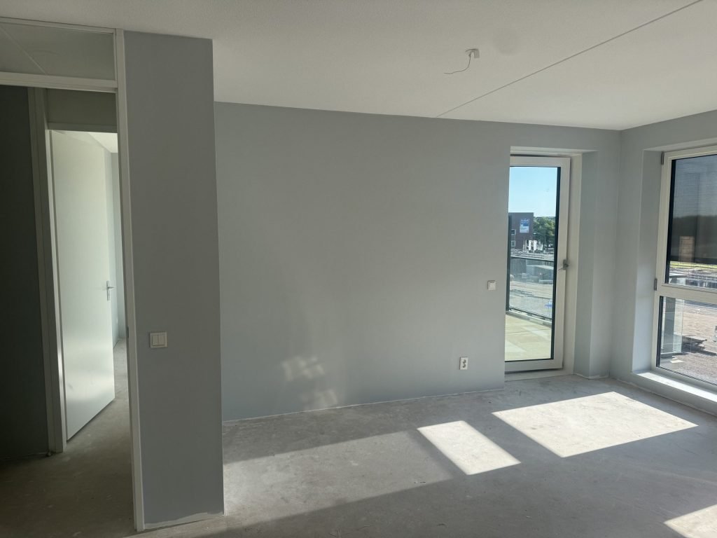 Opgeleverd nieuwbouwappartement met lichtgrijze wanden, een binnendeur en een balkondeur