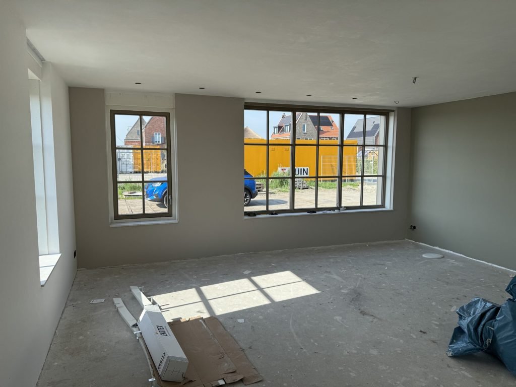 Woonkamer in een nieuw huis met grijsgroene wanden en grote ramen met roedeverdeling