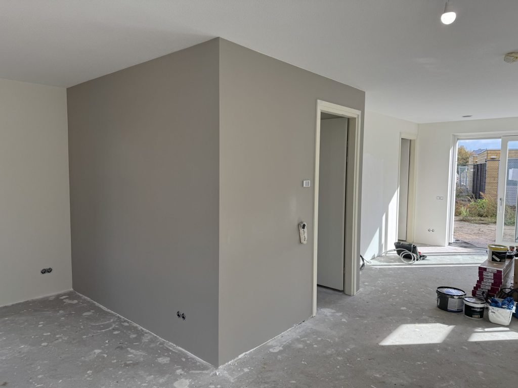 Nieuwbouwwoning met een pas afgewerkte grijze wand, binnendeur en verfemmers op de vloer
