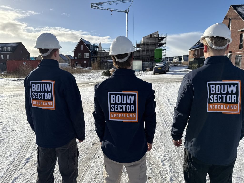 Drie vakmensen van Bouwsector Nederland met witte bouwhelm op een besneeuwde bouwplaats met nieuwbouwhuizen in aanbouw